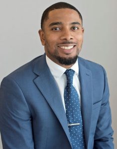 Profile portrait of Jujuan Lewis in a blue suit with blue and white tie.