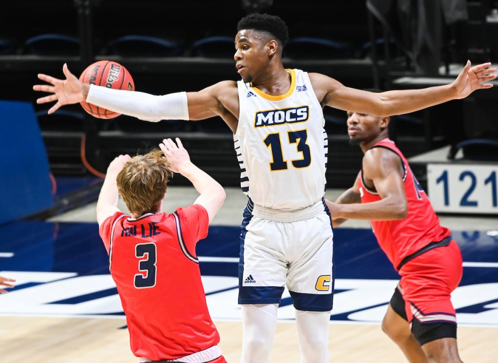 UTC basketball player reaching for basketball while guarded by Samford players.