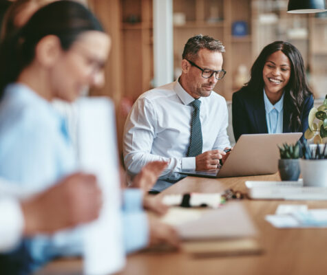 Two smiling diverse businesspeople using a laptop together at work. Flamingo Images/stock.adobe.com