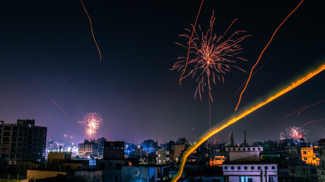 A horizontal view of a city at night with orange and pink fireworks in the sky.