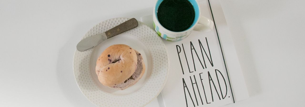 a cup of coffee, a planner, and a bagel