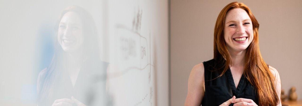 red-headed female teacher in front of a whiteboard