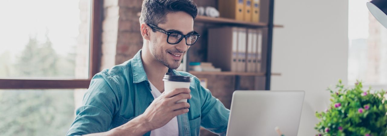 man drinking coffee and looking at his laptop