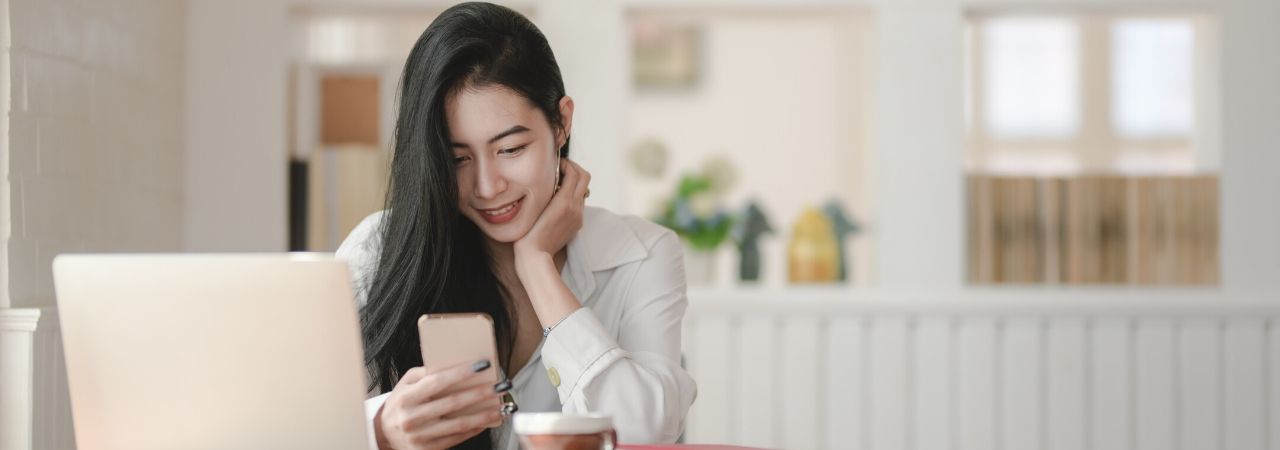 woman smiling looking at her phone by her laptop