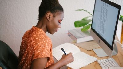 woman taking notes while sitting in front of her desktop computer