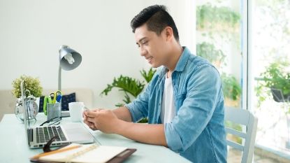 young man smiling and looking at his phone with his laptop open