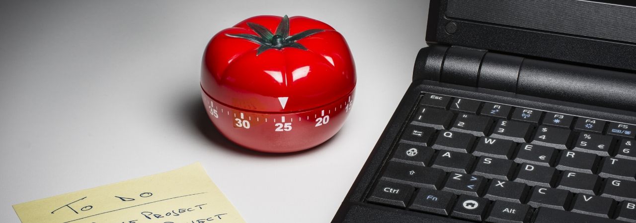 a tomato timer sitting between a black laptop and a to do list