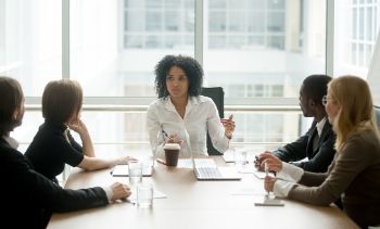 female leading in white shirt leading an office meeting with team members all wearing black