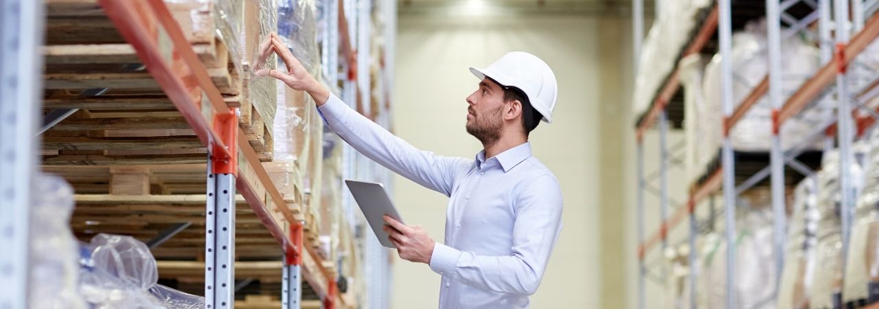 man in hard hat checking inventory in a warehouse using a tablet