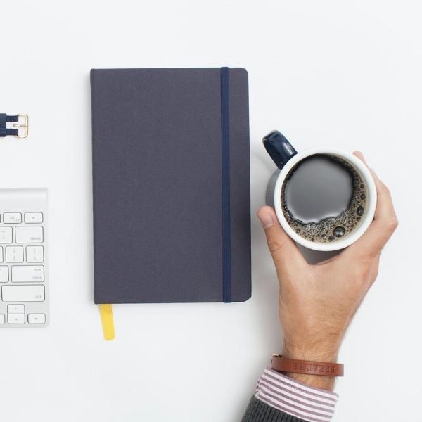 man typing on computer keyboard with one hand and holding black coffee in the other