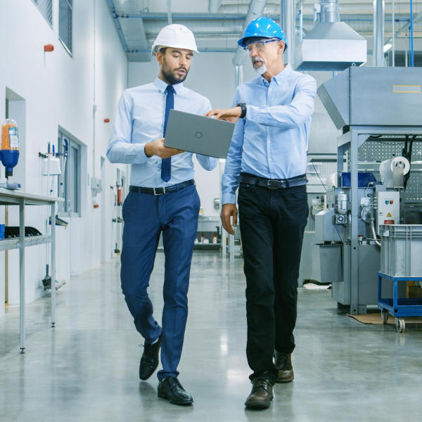 two male supply chain workers looking at a laptop while walking through a warehouse