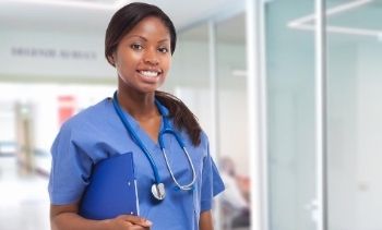 female medical assistant smiling in scrubs holding clipboard