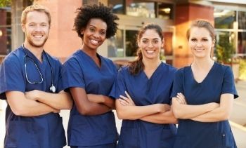 four members of a medical team smiling wearing blue scrubs