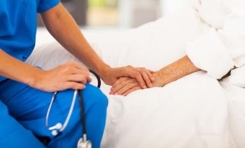medical assistant holding a senior patient's hand in their hospital bed