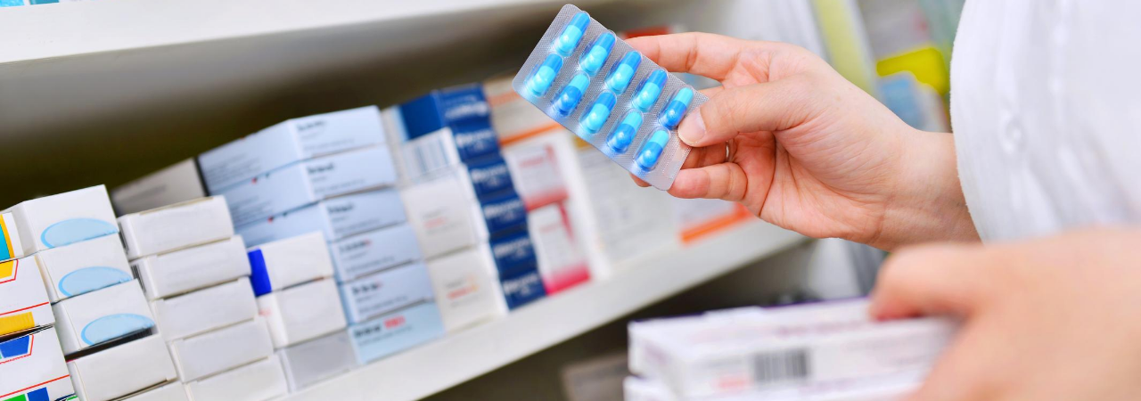 pharmacist holding blue pills and packaged medicine in their hands