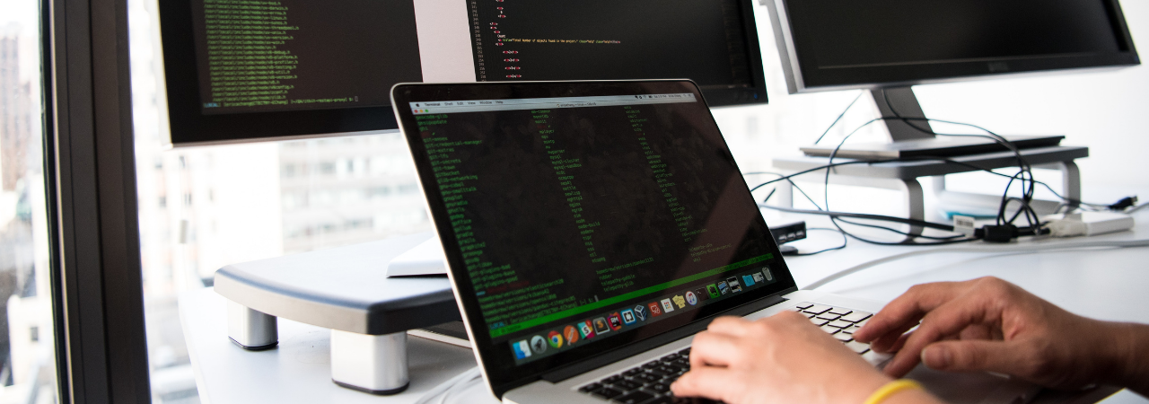 male typing on computer with multiple screens in background