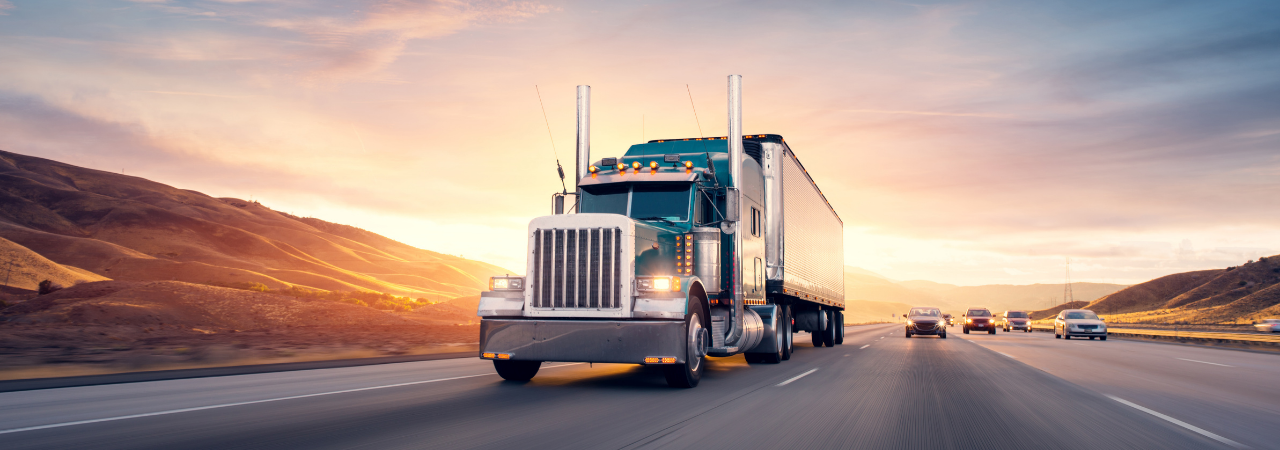 semi-truck driving on highway with sunset behind it