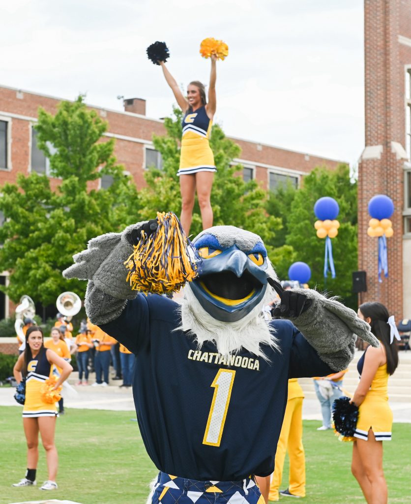 Color photograph of UTC mascot Scrappy Moc wearing a UTC jersey and waving a pom-pom. 