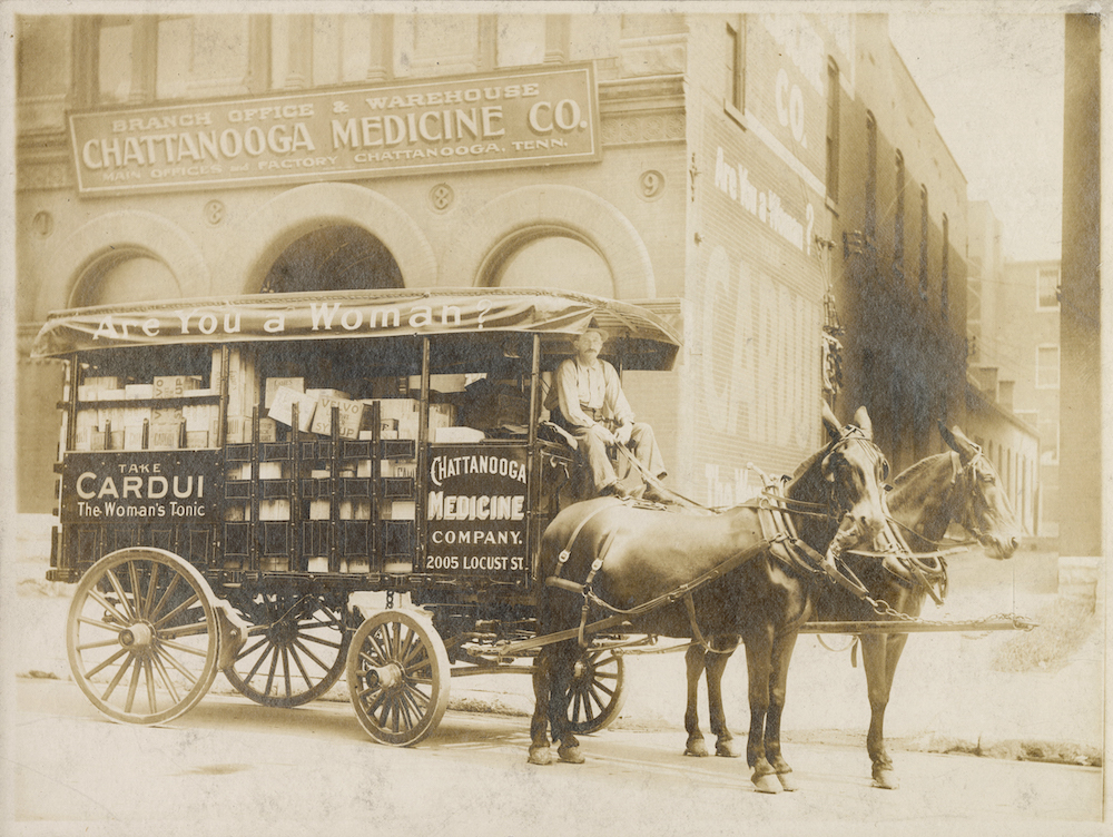 Black-and-white photograph of Chattanooga Medicine Company wagon. The wagon has advertising that reads "Are You a Woman? Take CARDUI The Woman's Tonic CHATTANOOGA MEDICINE COMPANY. 2005 LOCUST ST." Behind the wagon is a printed sign that reads "BRANCH OFFICE & WAREHOUSE CHATTANOOGA MEDICINE CO. MAIN OFFICE AND FACTORY CHATTANOOGA, TENN.