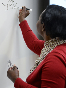 African American lady writes on white board in classroom