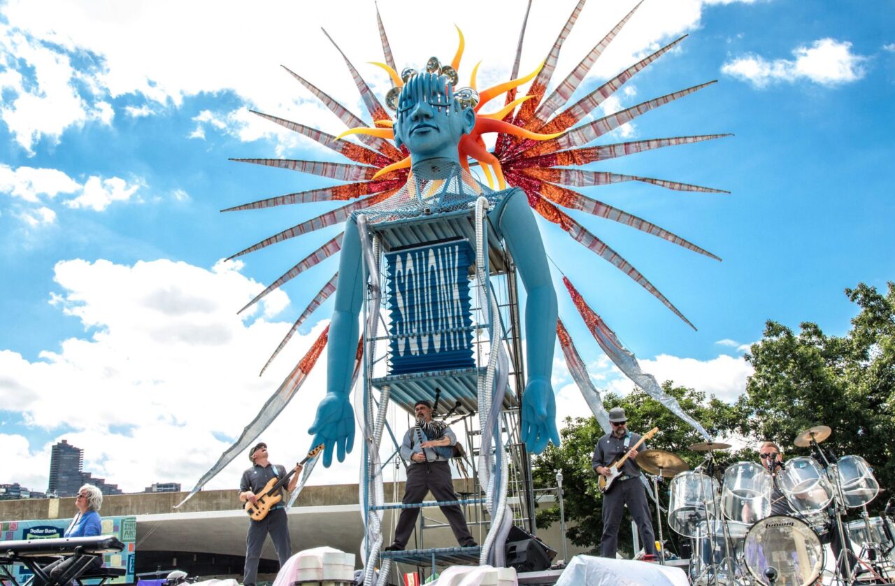 Guitarists in front of large art piece on stage shaped like a robot