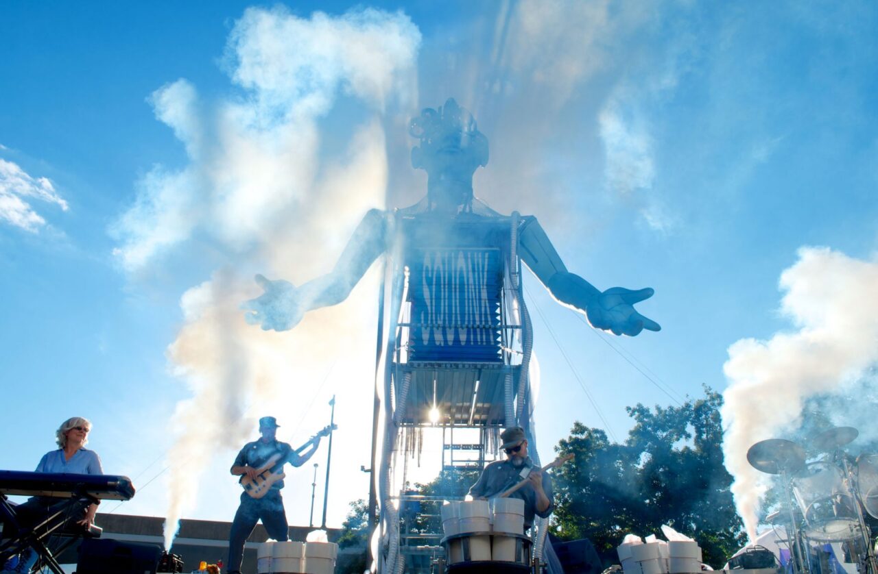 Stage show with musicians playing guitar in front of large art piece