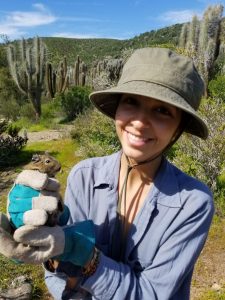 Grillo holds a 'goo ub her hands. There's a view of the parks landscape, with cactuses and shrubs behind her.