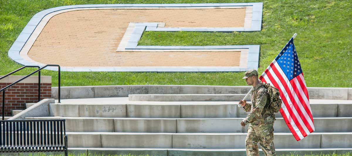 rots student carries American flag in front of large power C at 9/11 remembrance event