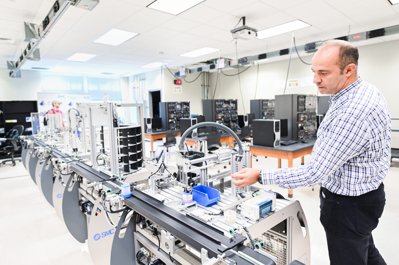 Erkan Kaplanoglu, professor of mechantronics, stands at the end of the production line in the mechatronics lab. The line is a smaller version of the ones used in real-world factories.