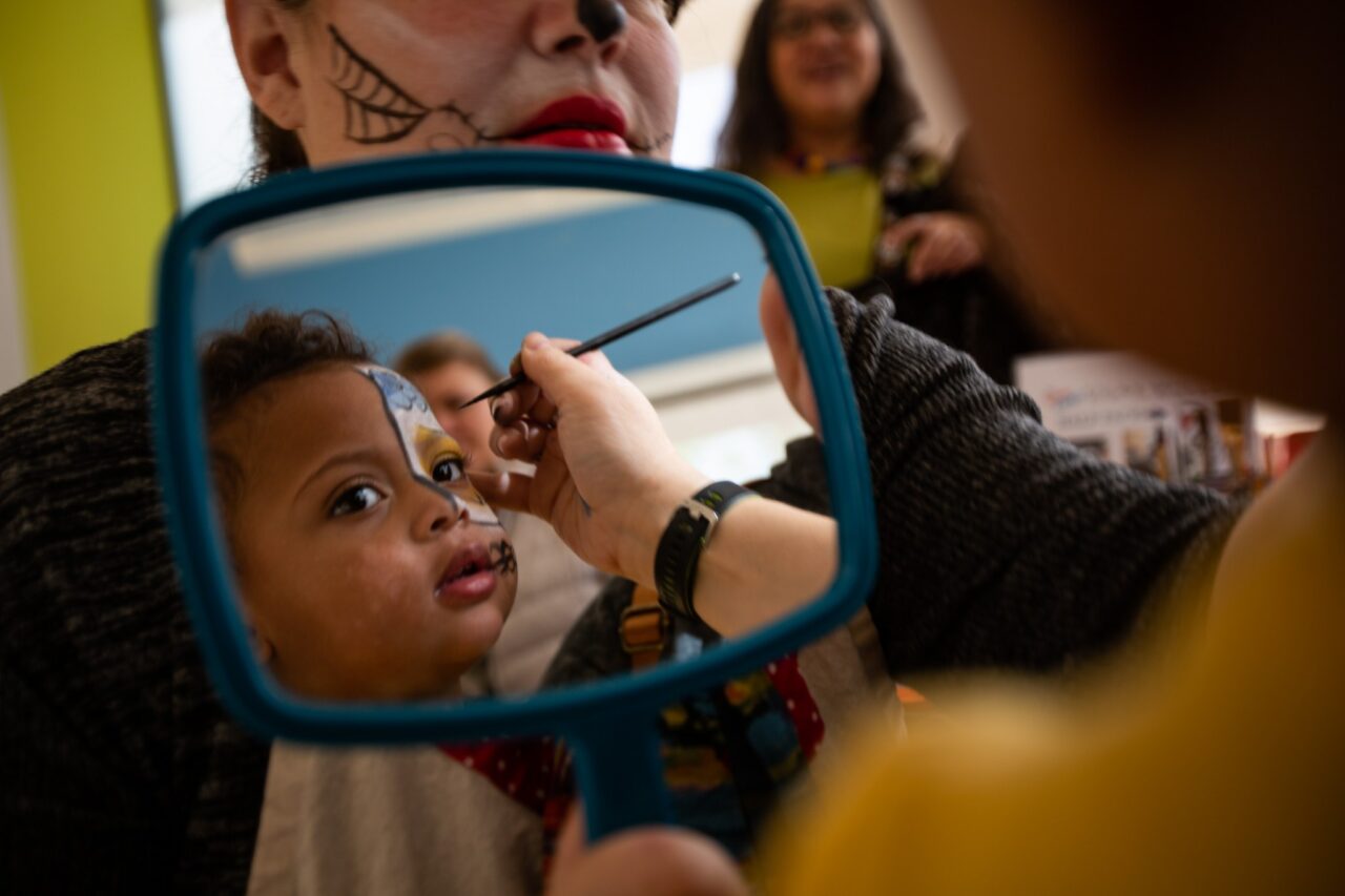 Troy Stolt photo: Trinity Rodriguez-Clynes, 1, of Crestwood, Missouri, looks into the mirror as she gets her face painted during the Dia de los Muertos celebration at the Missouri History Museum. Photo courtesy St. Louis Post-Dispatch.