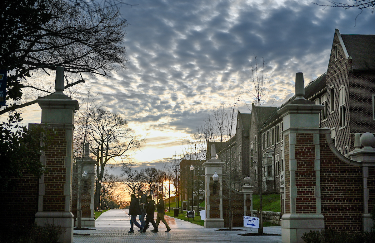 A group of students walk under large clouds on oak street near founders hall.