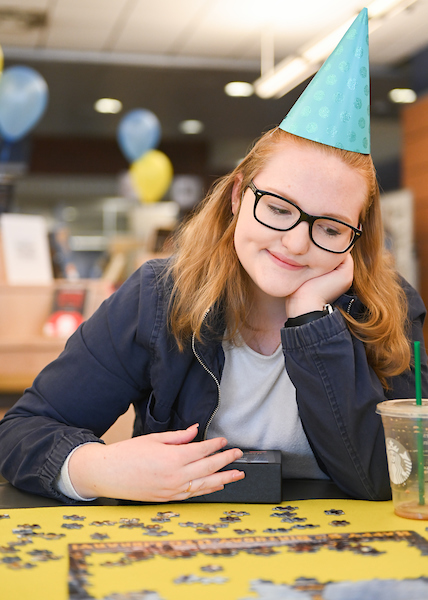 A UTC student in a birthday hat looks at a puzzle.