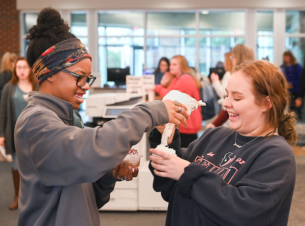 Two students laugh while putting icing on a cupcake.