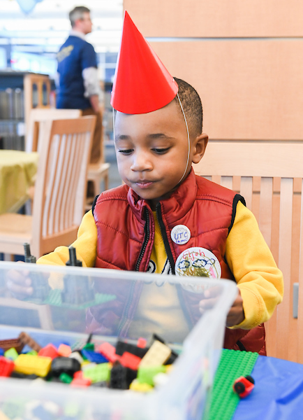 A small boy in a birthday hat plays with legos.