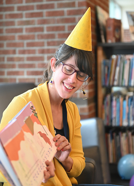 A woman with a birthday hat on reads a children's book.
