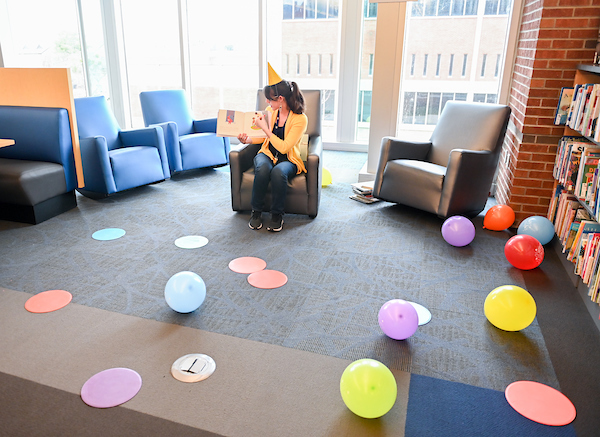 A woman in a birthday hat reads a book aloud in the library