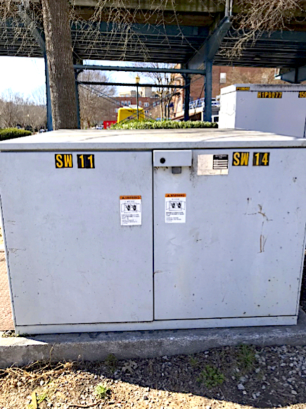 A large blank electrical box is on the ground under a bridge.