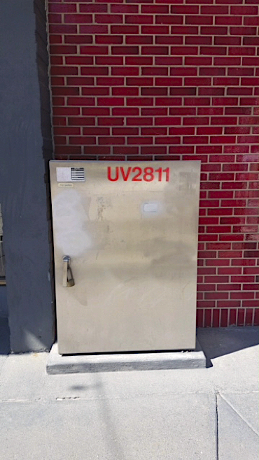 A blank electrical box is flush with a brick wall.