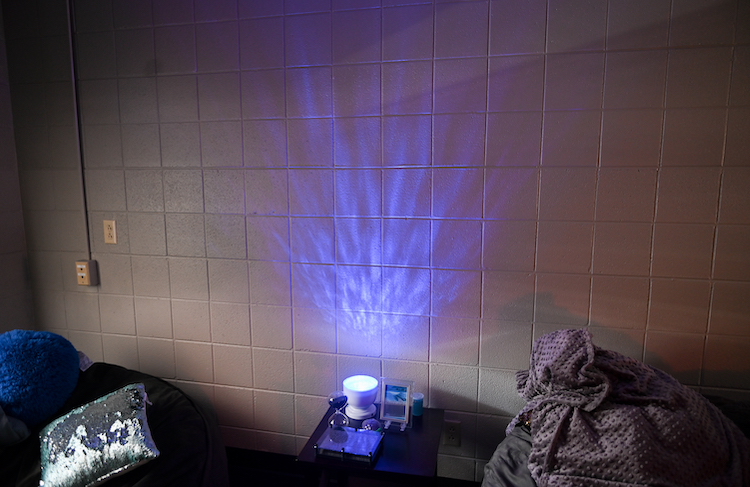 A blue light sits in between a pillow and purple blanket