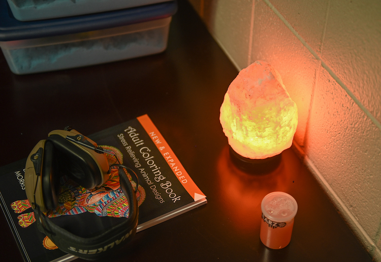 A pair of headphones lays on top of an adult coloring book, next to a salt lamp and a container of putty.