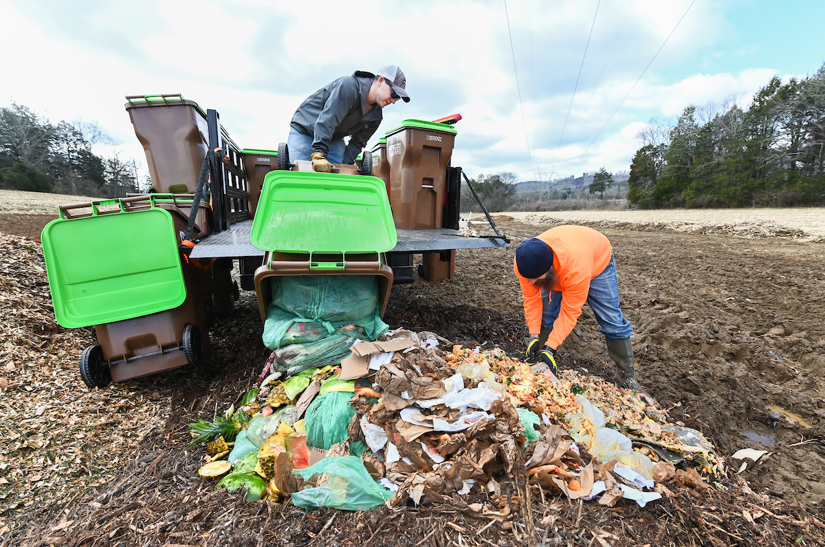 Michael Ryan, orange jacket, sifts through a pile of food scraps to remove anything that can't be composted.