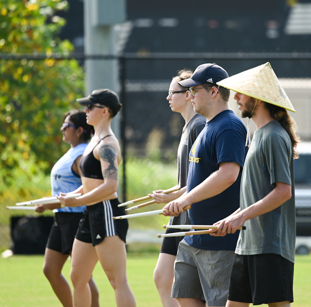 Students from UTC's Marching Mocs stand in line outdoors, each holding drumsticks.