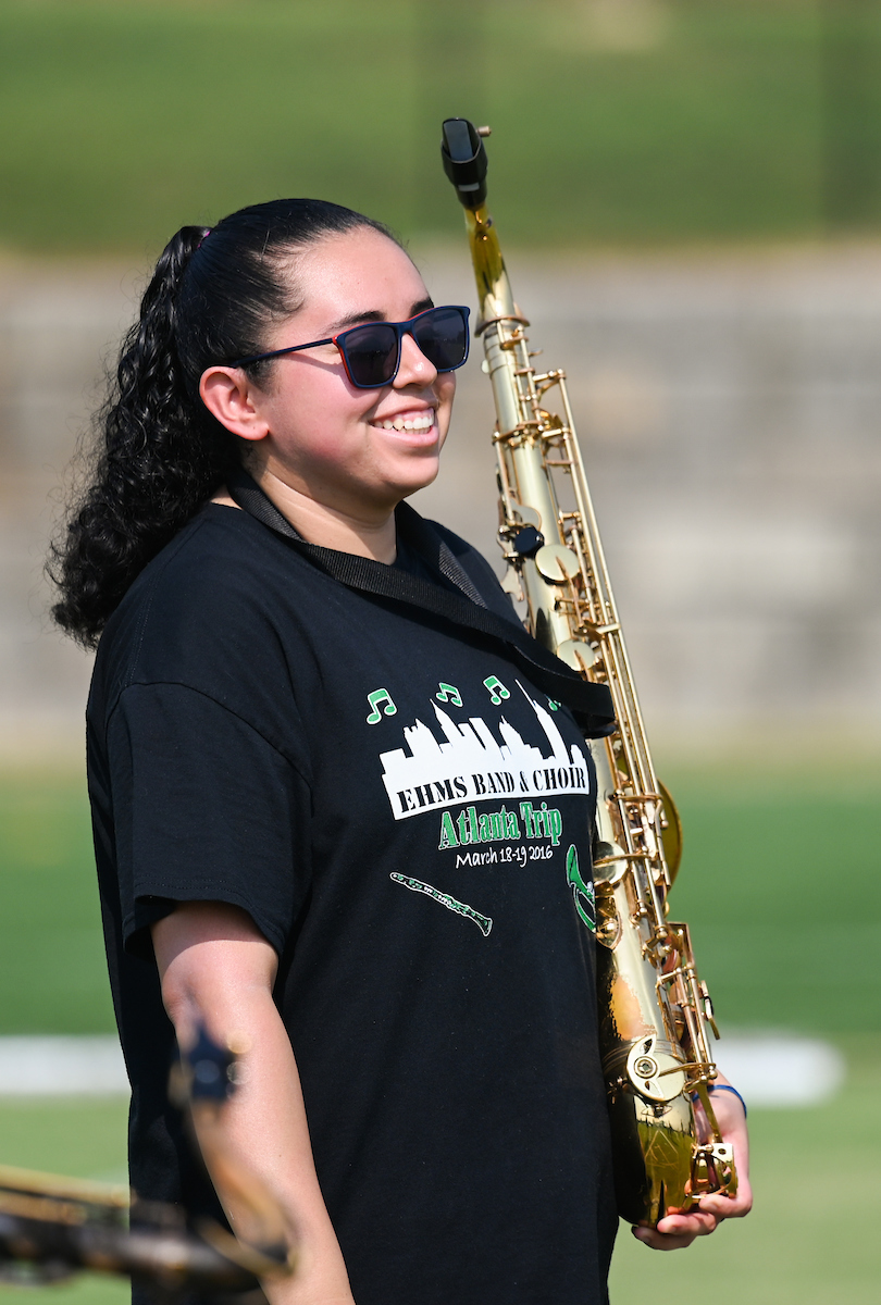 Marching Mocs member smiles while holding a saxophone, on a sports field.