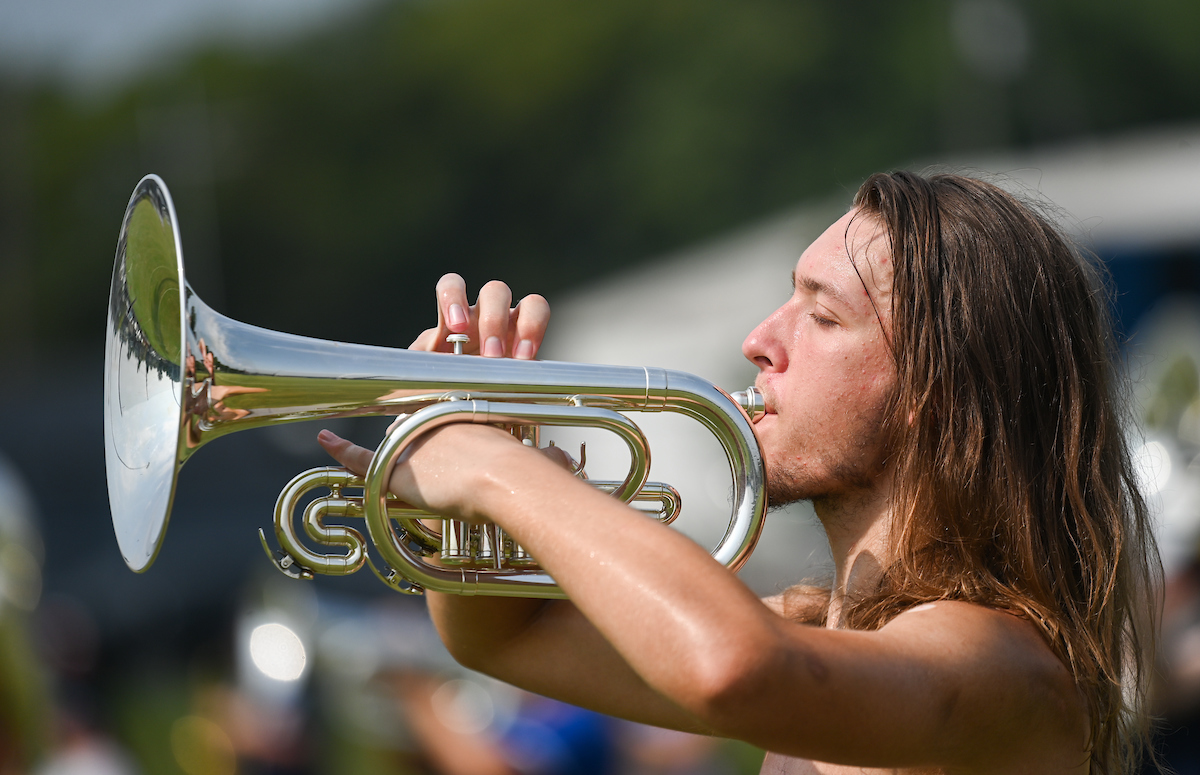 Marching Mocs member plays a shiny brass instrument outdoors.