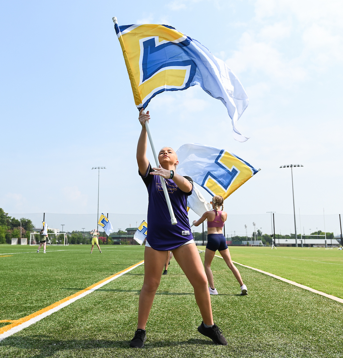 Marching Mocs members wave a large blue and yellow flag on a sports field.