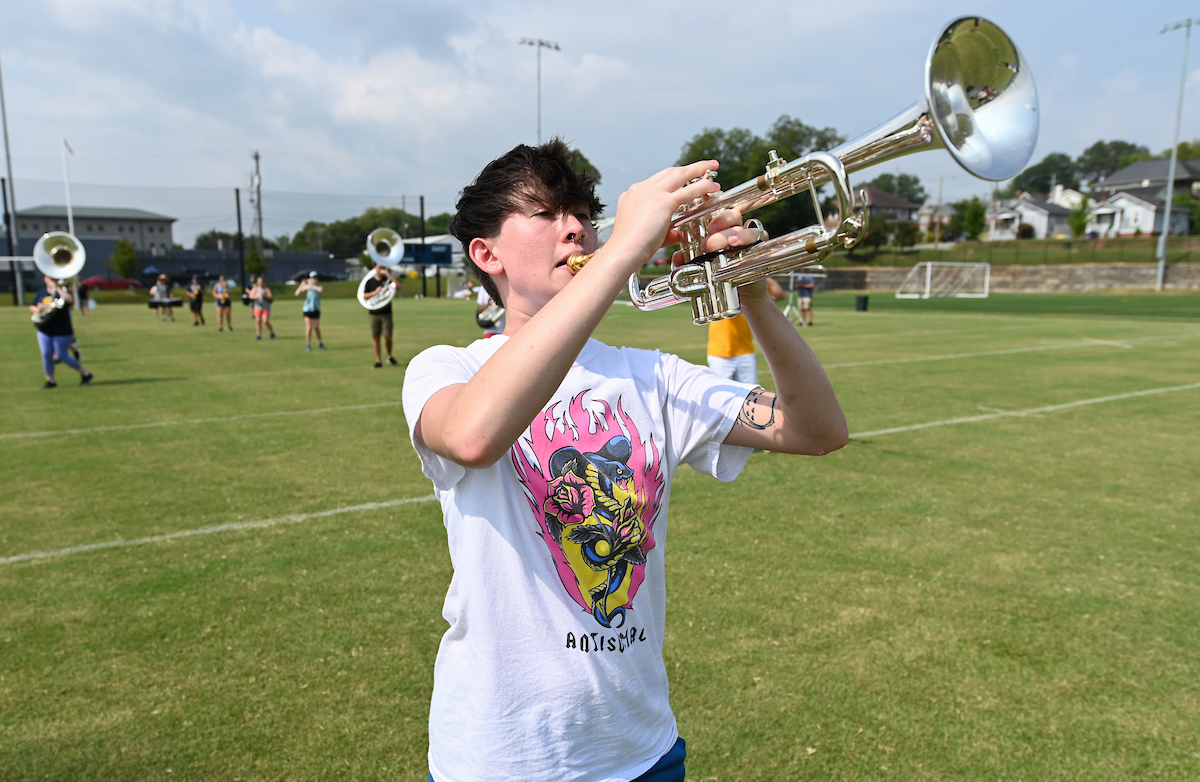 Marching Mocs member plays trumpet on a grassy field.