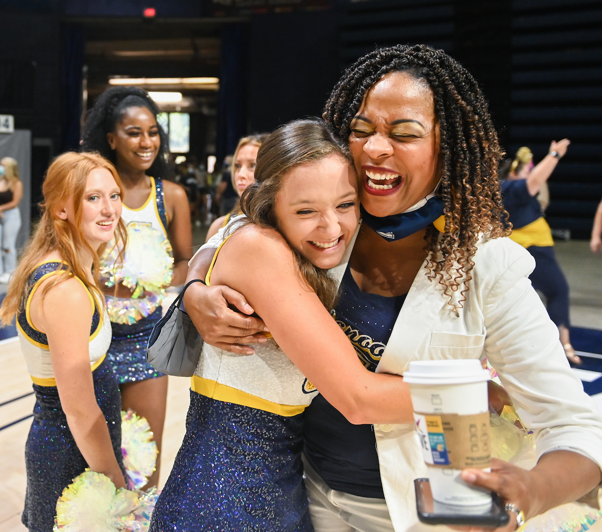 A woman hugging a dancer, both smiling. Group of dancers in the background.