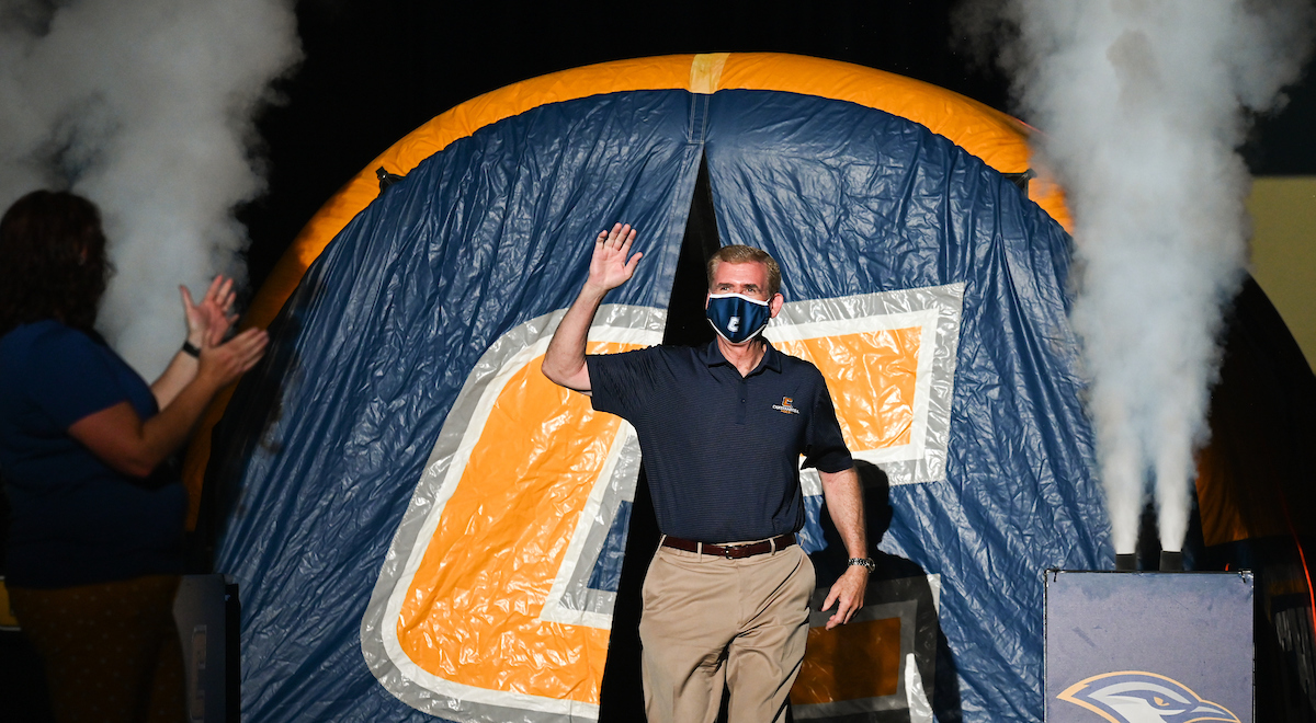 Chancellor Dr. Steven R. Angle walking out of the tunnel with a power "C" on it and waving to the crowd. Fog billows beside him.