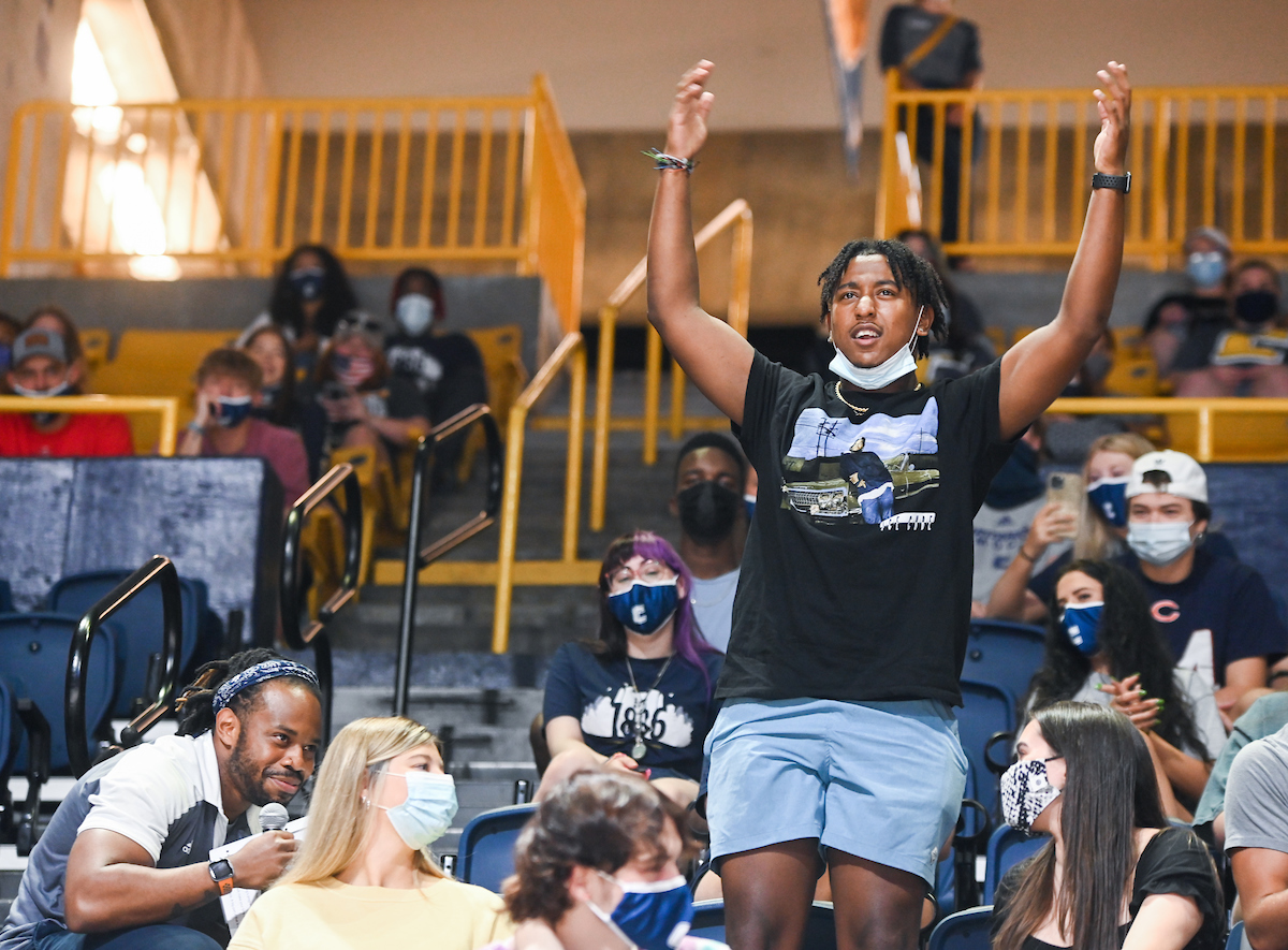 Student stands with arms raised, surrounded by masked students in the McKenzie Arena.