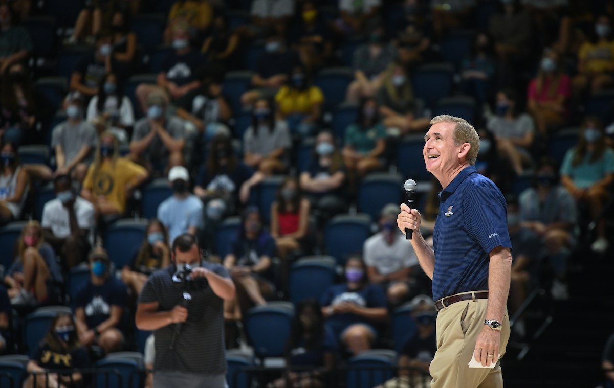 A man holding a microphone, standing before a crowd at the McKenzie Arena.